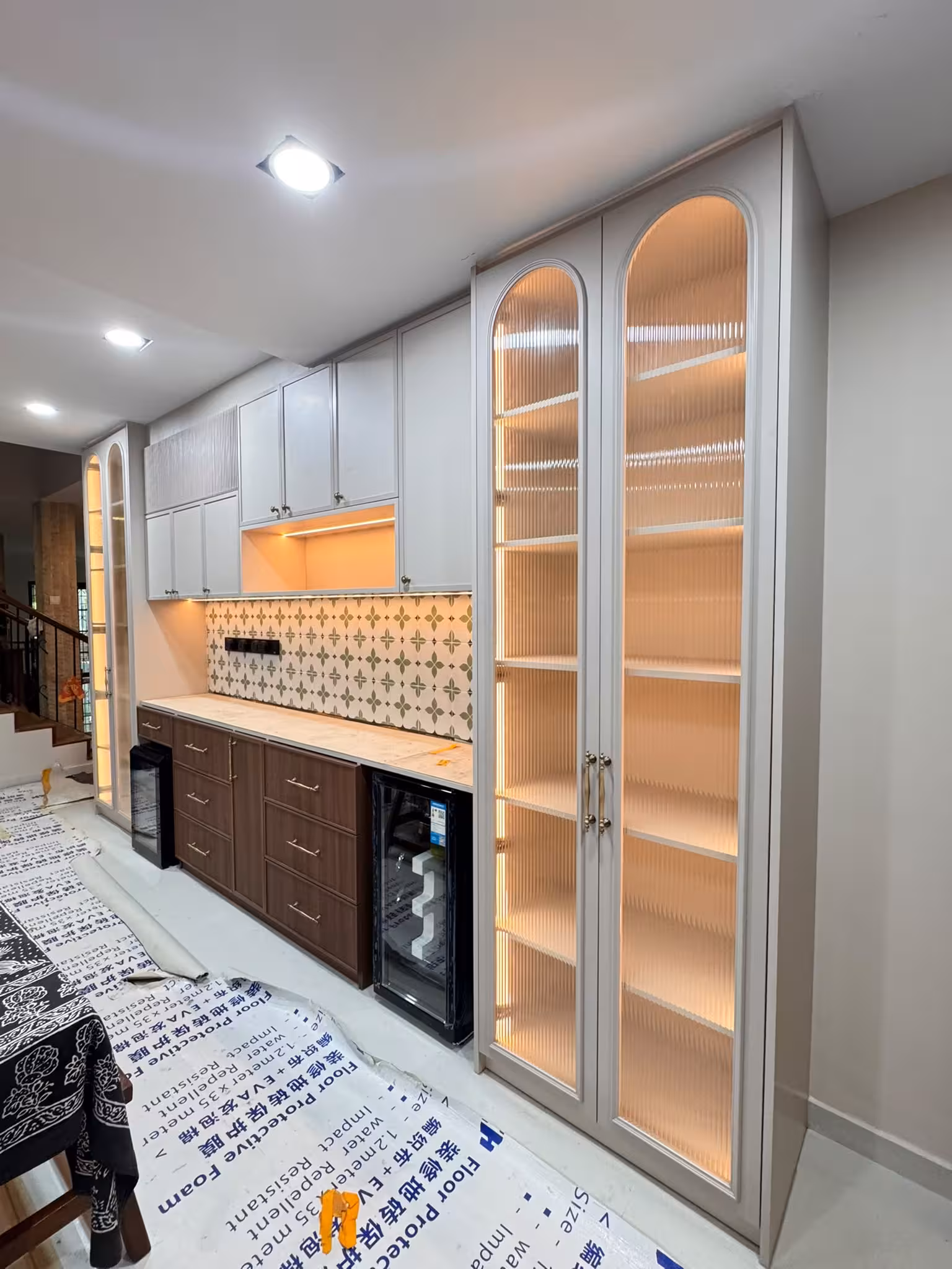 Tse7en built-in display cabinet with illuminated fluted glass panels, upper storage cabinets, and wood drawers with patterned tile backsplash